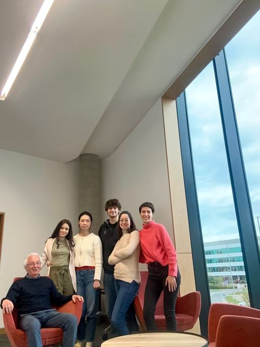 David Winter seated with students of the programme in front of a window at the University of Hertfordshire